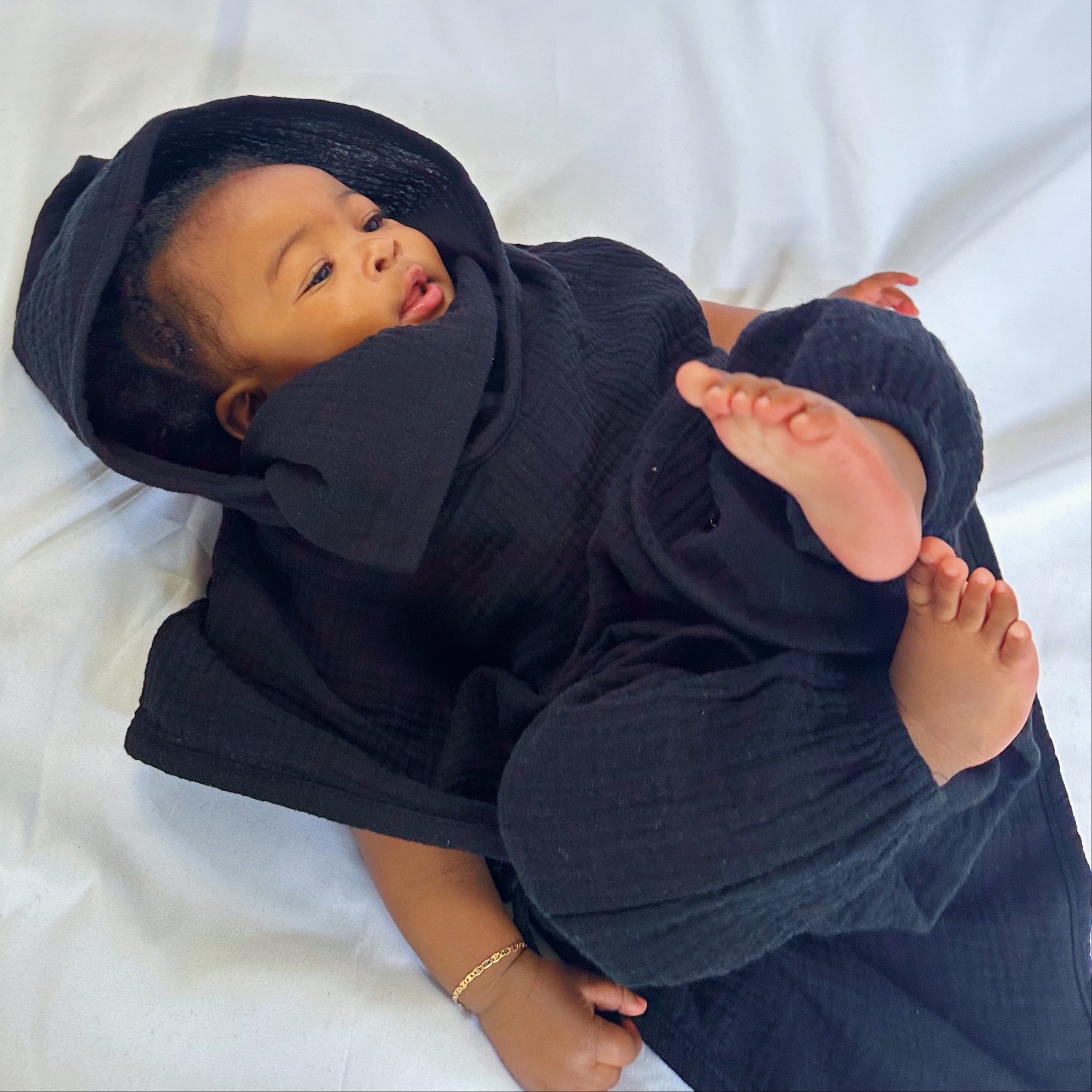 Baby wrapped in a black blanket and hat on a white background